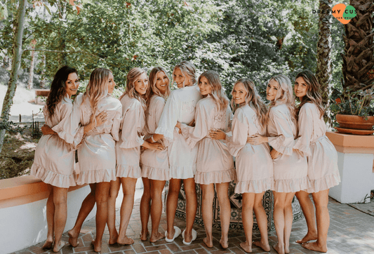 A joyful bridal party poses in matching pink robes with the bride in white, capturing a beautiful and coordinated pre-wedding moment.