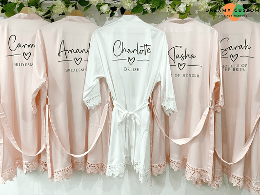 Batas personalizadas de satén con encaje para la novia y su séquito. Diseñadas con nombres y roles bordados, estas elegantes batas añaden un toque especial a la preparación del gran día.