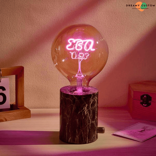 Una bombilla de filamento personalizada con luz rosa vibrante, montada sobre una base de mármol elegante. Un regalo original y significativo, ideal para bodas de oro, aniversarios o decoración especial.