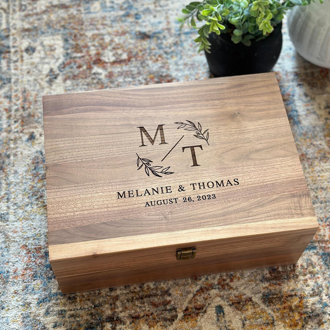 This image shows a personalized engraved wooden memory box, featuring the initials "M/T" and the names "Melanie & Thomas" along with their wedding date, "August 26, 2023." It's a thoughtful keepsake for special moments.