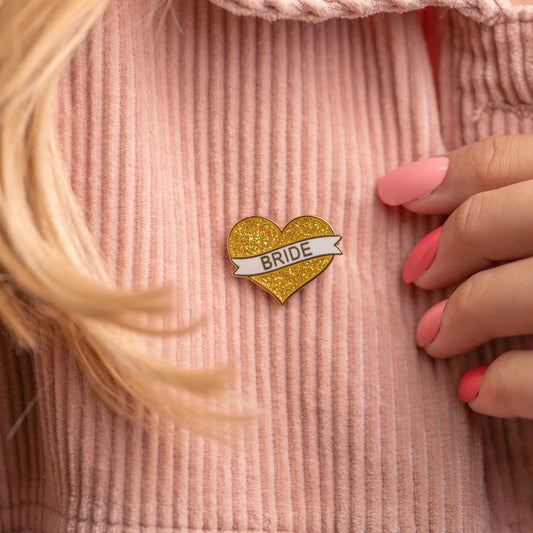 This glittery "Bride" heart pin is the perfect accessory to showcase the bride-to-be's special role. A lovely and fun keepsake for the bride to wear leading up to her big day.