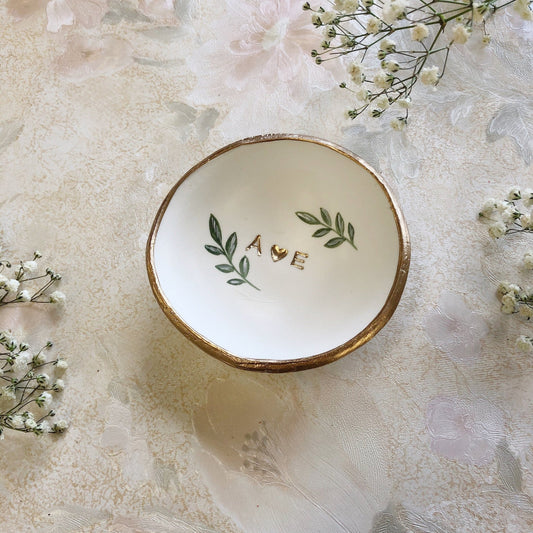This personalized jewelry dish, featuring the initials "A♥E" and delicate green leaves with a gold rim, makes a thoughtful and elegant gift, perfect for celebrating special moments and cherished memories.