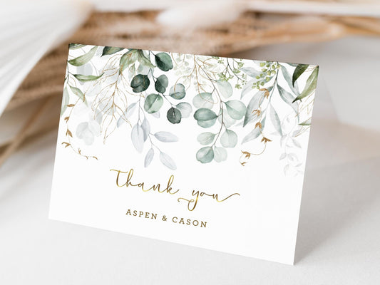 The image features a beautiful custom wedding thank-you card adorned with delicate watercolor greenery and gold accents. The card reads "Thank you" with the names "Aspen & Cason" printed elegantly beneath.