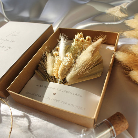 A beautifully arranged dried flower bouquet in a kraft gift box, featuring a romantic message in German, perfect for a wedding celebration. This elegant bouquet is a sustainable, lasting option for modern couples.