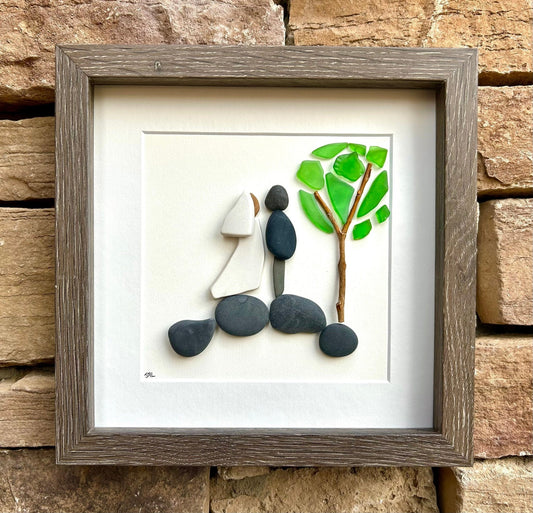 A beautiful piece of pebble art featuring a couple, with a tree made from glass and sticks, framed elegantly—perfect for wedding décor or a meaningful gift that captures a special moment.