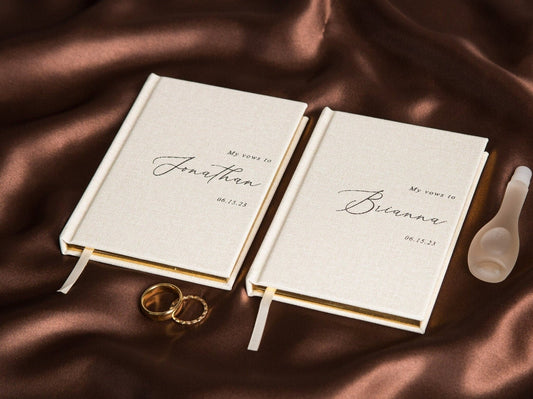 This image shows elegant personalized vow books with gold-edged pages. The books are labeled "My Vows to Jonathan" and "My Vows to Brianna," perfect for wedding vows, accompanied by wedding rings and a perfume bottle.