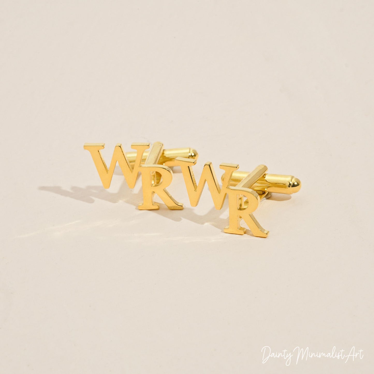 Close-up of gold "WR" initial cufflinks on a beige background.