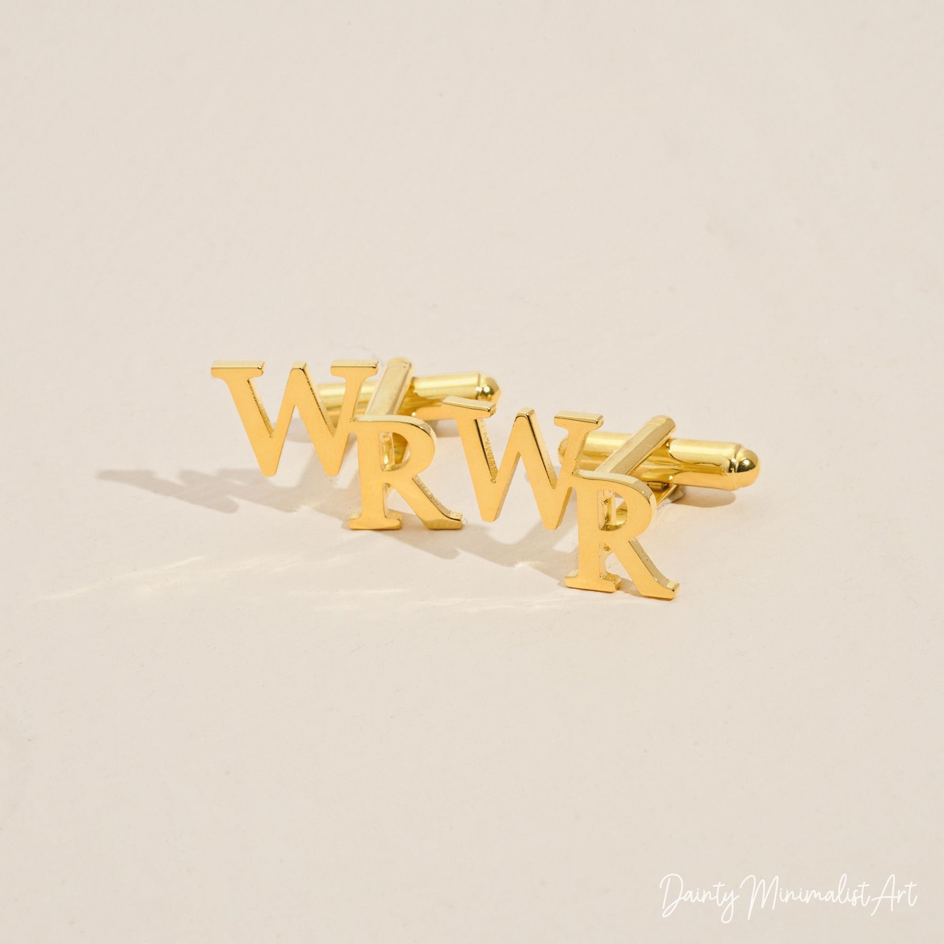 Close-up of gold "WR" initial cufflinks on a beige background.