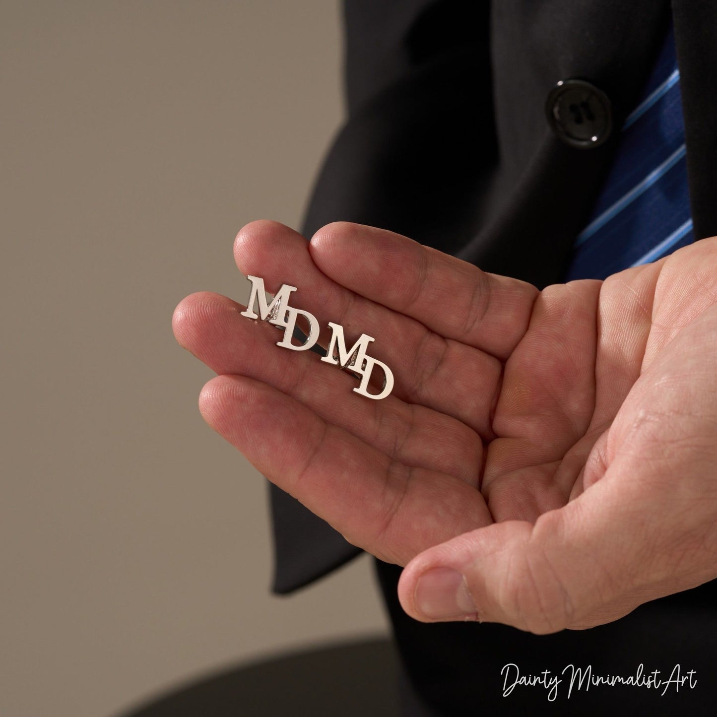 A pair of silver "MD" initial cufflinks held in hand.