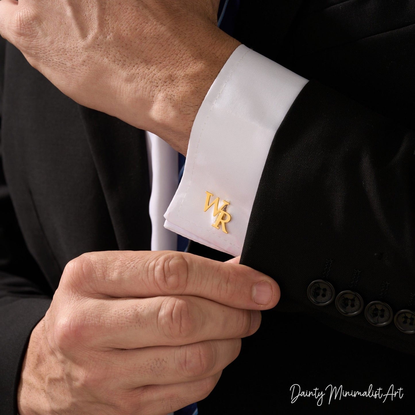 A man wearing gold "WR" initial cufflinks on his white shirt cuff.