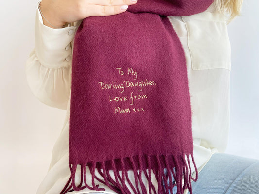 A person wearing a white sweater holds a red personalized scarf with the embroidered message "To My Darling Daughter, Love from Mum xxx" on it.