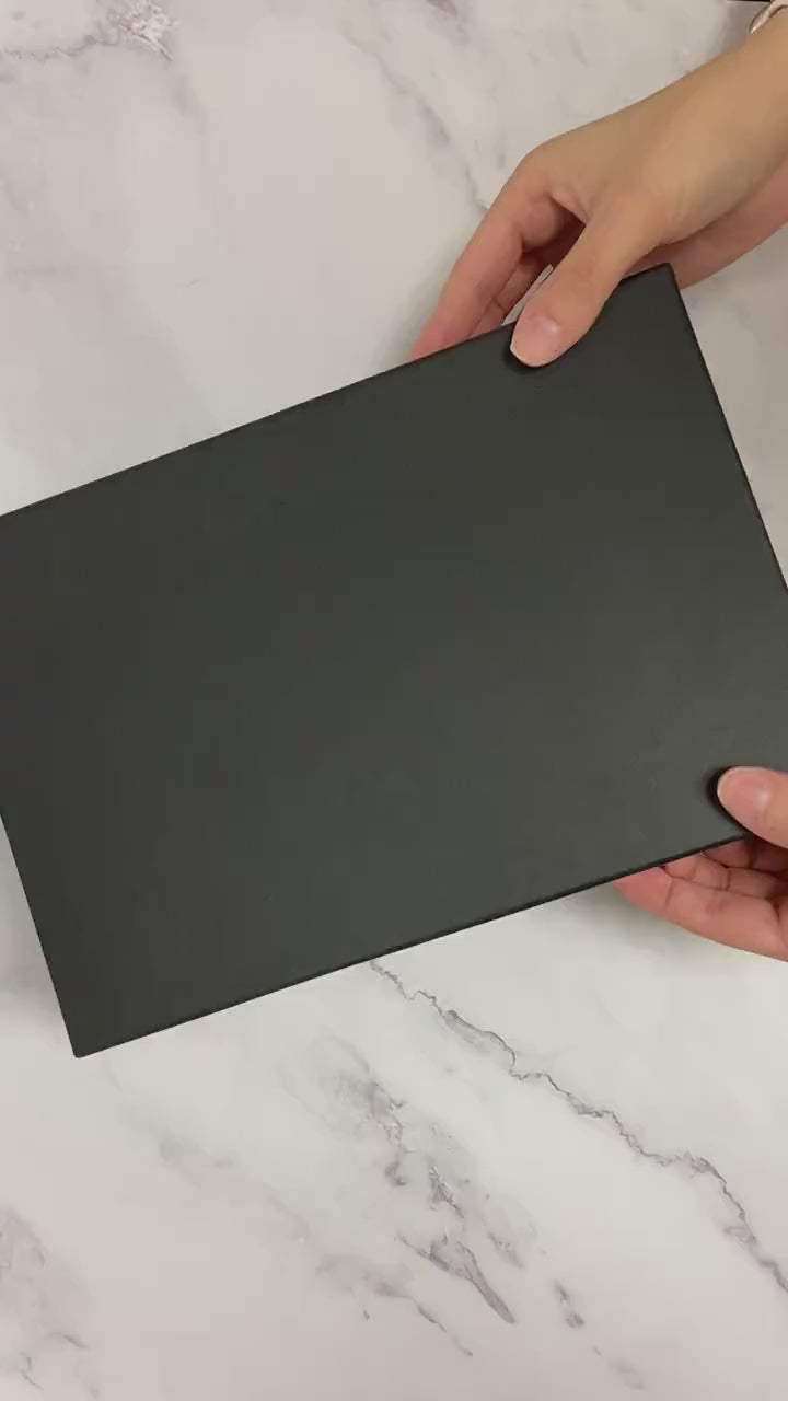 Close-up of hands opening a black gift box containing a set of custom wedding champagne flutes with engraved names.