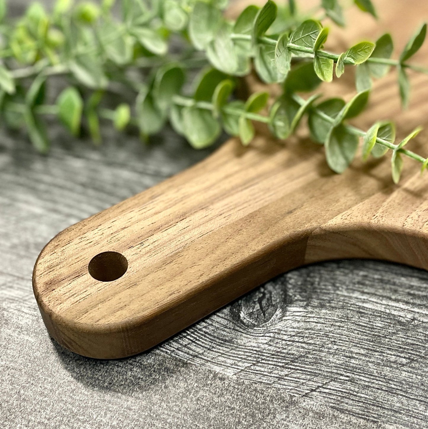Close-up of the handle on a walnut monogrammed charcuterie board, featuring a smooth finish and hanging hole.