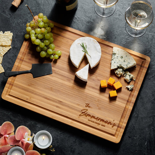 Engraved charcuterie board beautifully arranged with cheeses, grapes, and wine, ideal for entertaining.