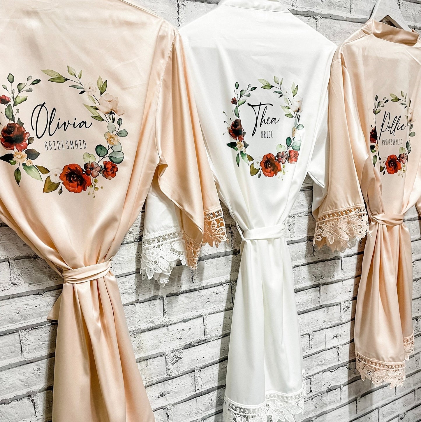 Personalized bridesmaid robes in peach and white: Luxurious satin robes with floral prints and custom names 'Olivia,' 'Thea,' and 'Millie' for a wedding party.