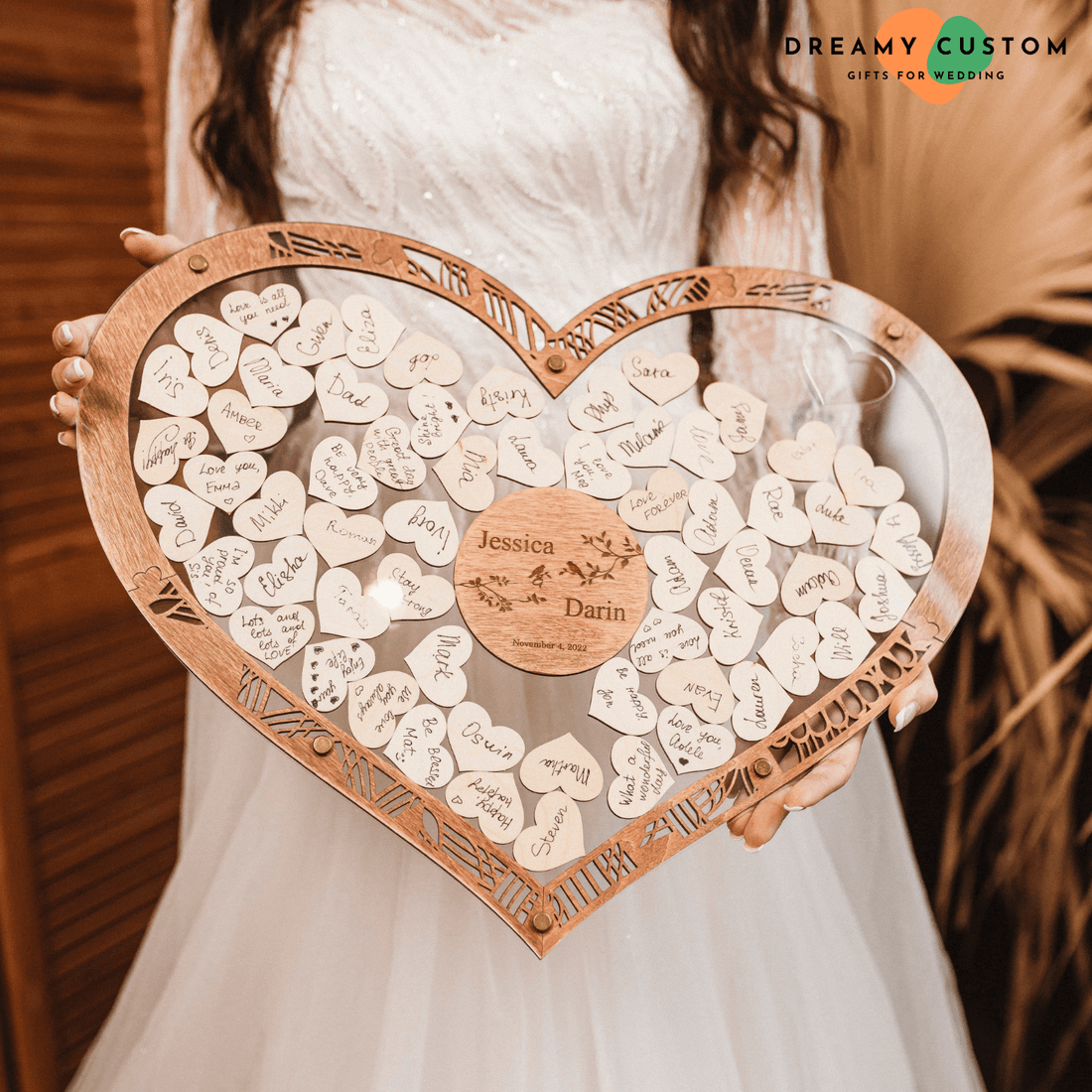 Libro de visitas de boda en forma de corazón con nombres personalizados. Cada invitado deja un mensaje en pequeños corazones de madera, creando un recuerdo emotivo y único para la pareja.