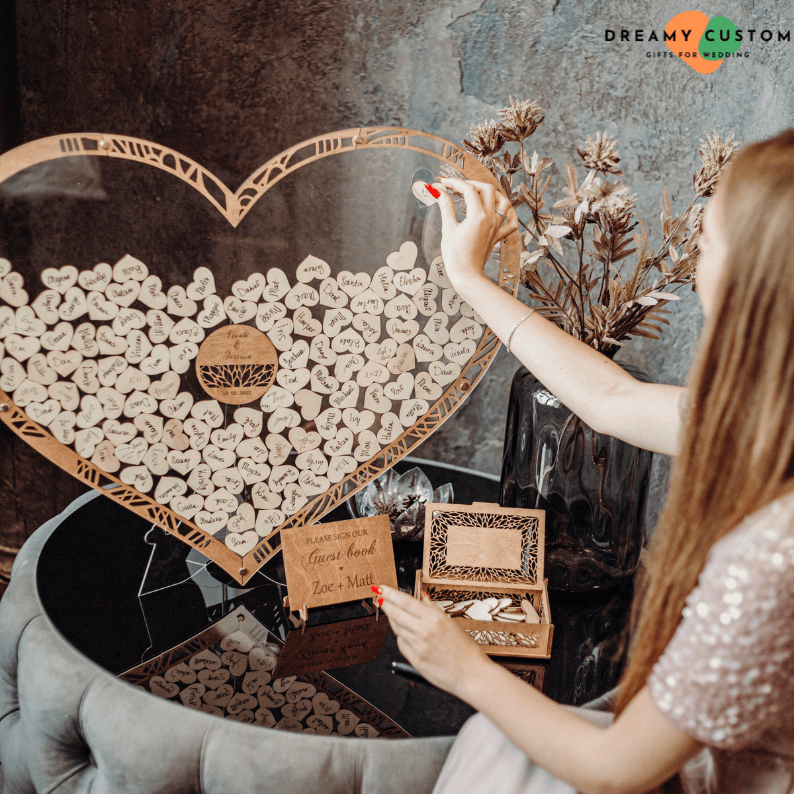 A wedding guest adds a heartfelt message to a wooden heart guest book, a unique and personalized alternative to traditional sign-in books. This elegant keepsake preserves special wishes from loved ones forever.