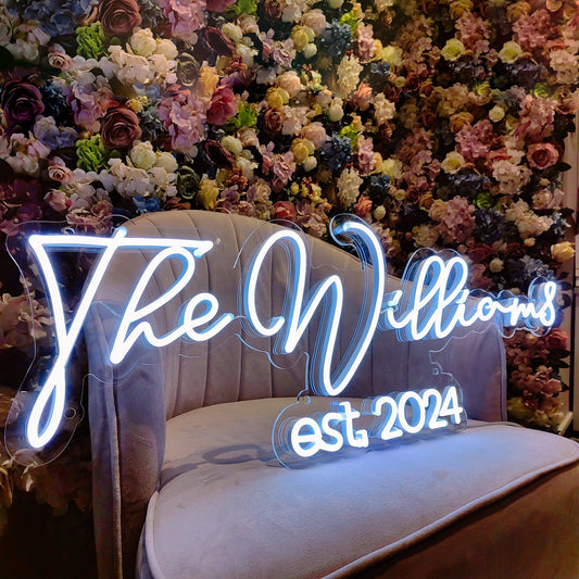 Personalized LED wedding sign with "The Williams est. 2024" glowing against a floral backdrop.