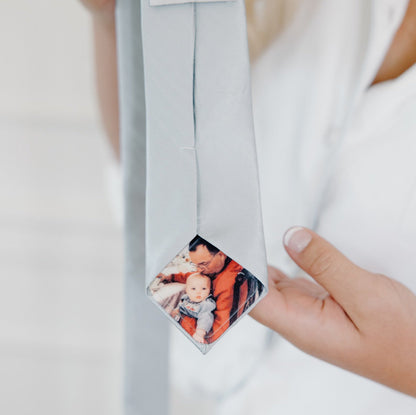 Close-up-of-a-custom-photo-tie-patch-on-a-light-gray-tie-held-by-a-bride-and-her-father.