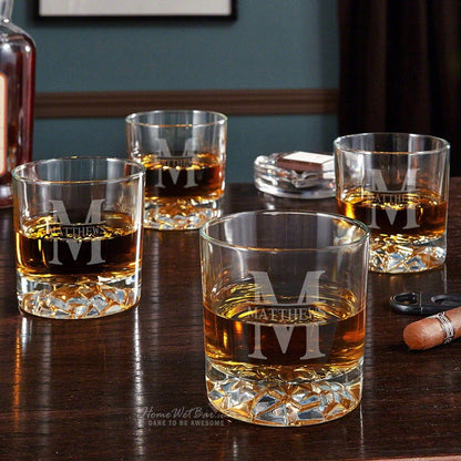 Collection of four personalized engraved whiskey glasses, each elegantly designed, placed on a home bar setting ideal for gifting.