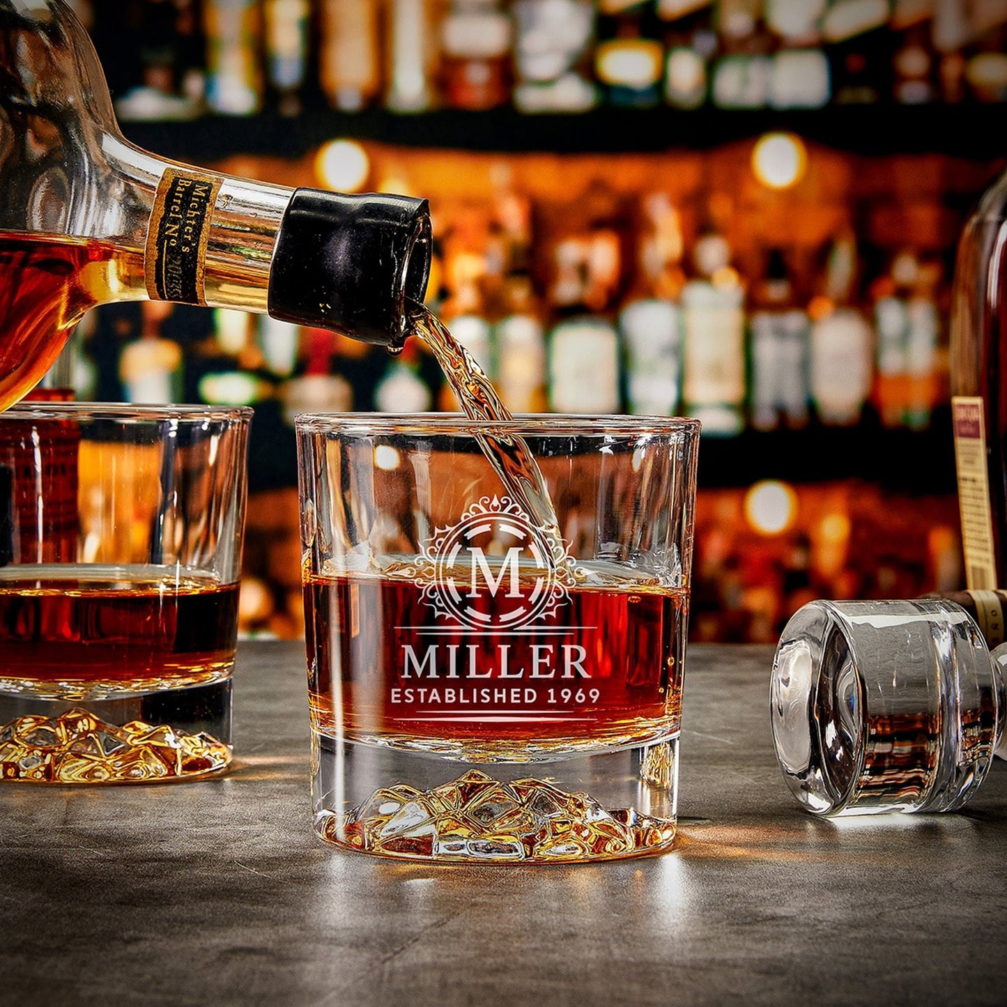 Personalized engraved whiskey glass with "Miller" design, bourbon being poured into it, showcasing elegant glacier-style base.