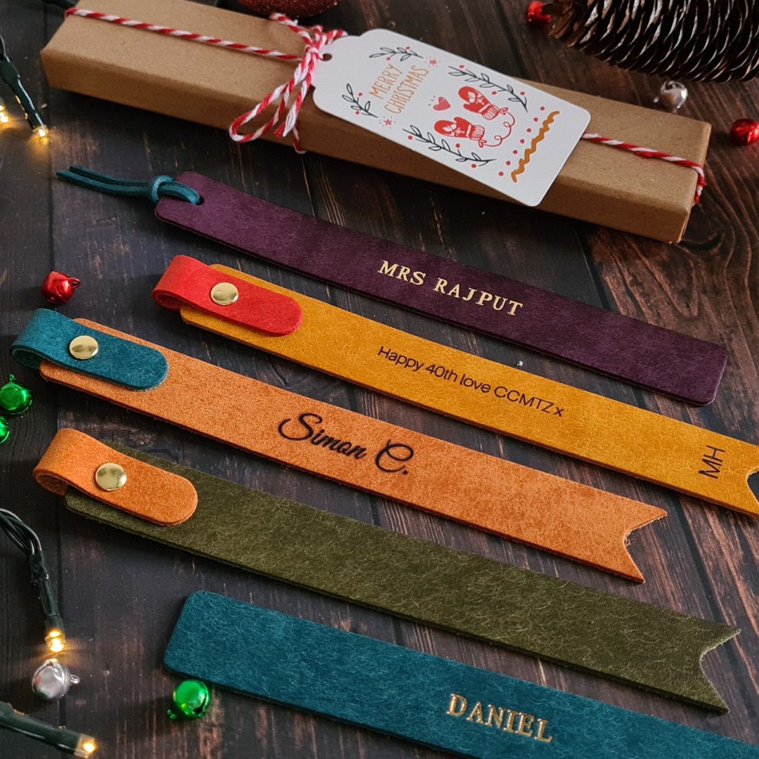 Set of personalized leather bookmarks in different colors with gold or embossed text, ideal for book lovers.