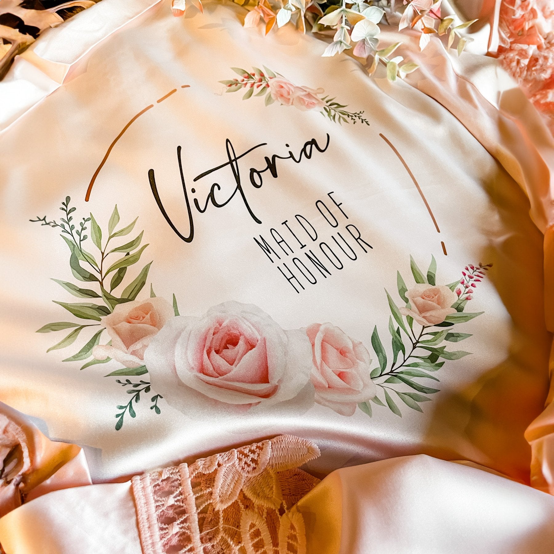 Victoria maid of honour personalized robe: A detailed view of a custom satin robe in cream with pink floral accents and the name 'Victoria' for the maid of honour.