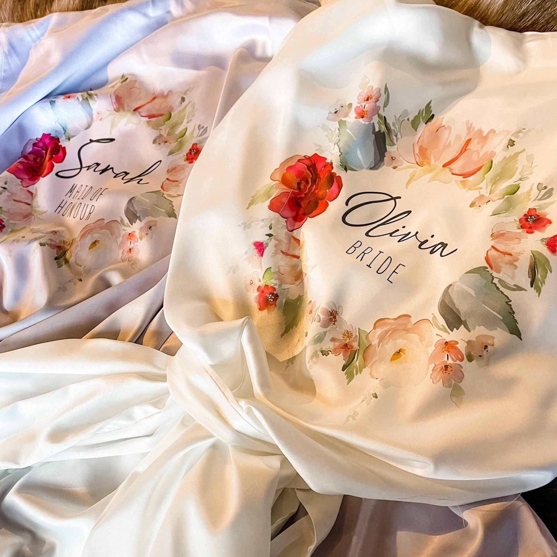 Bridal and maid of honour robes with floral wreaths – Luxurious satin robes with soft watercolor floral accents, custom-printed with names 'Sarah' (Maid of Honour) and 'Olivia' (Bride).