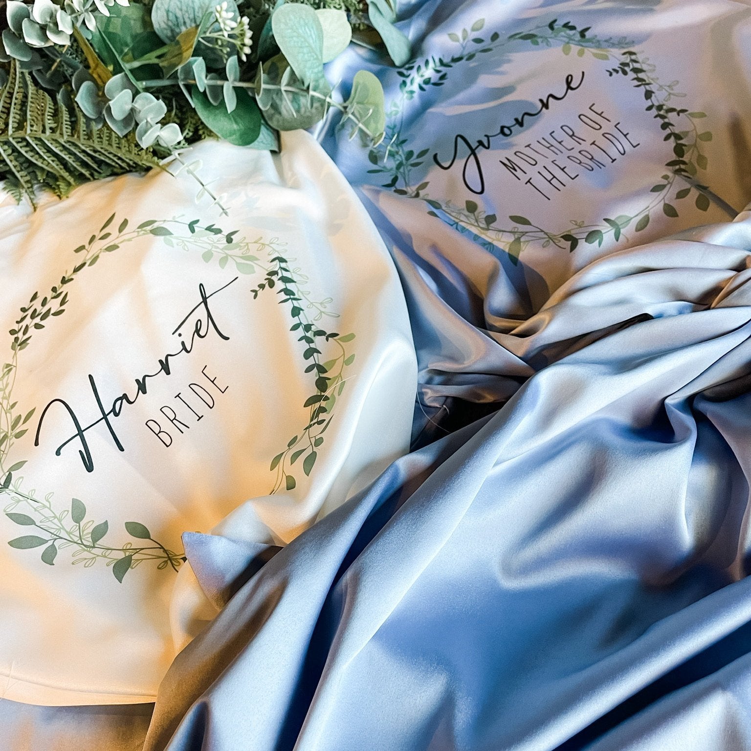 Detailed view of personalized bridal robes: Close-up of satin robes in sage green and blue with custom embroidery for the bride and mother of the bride.